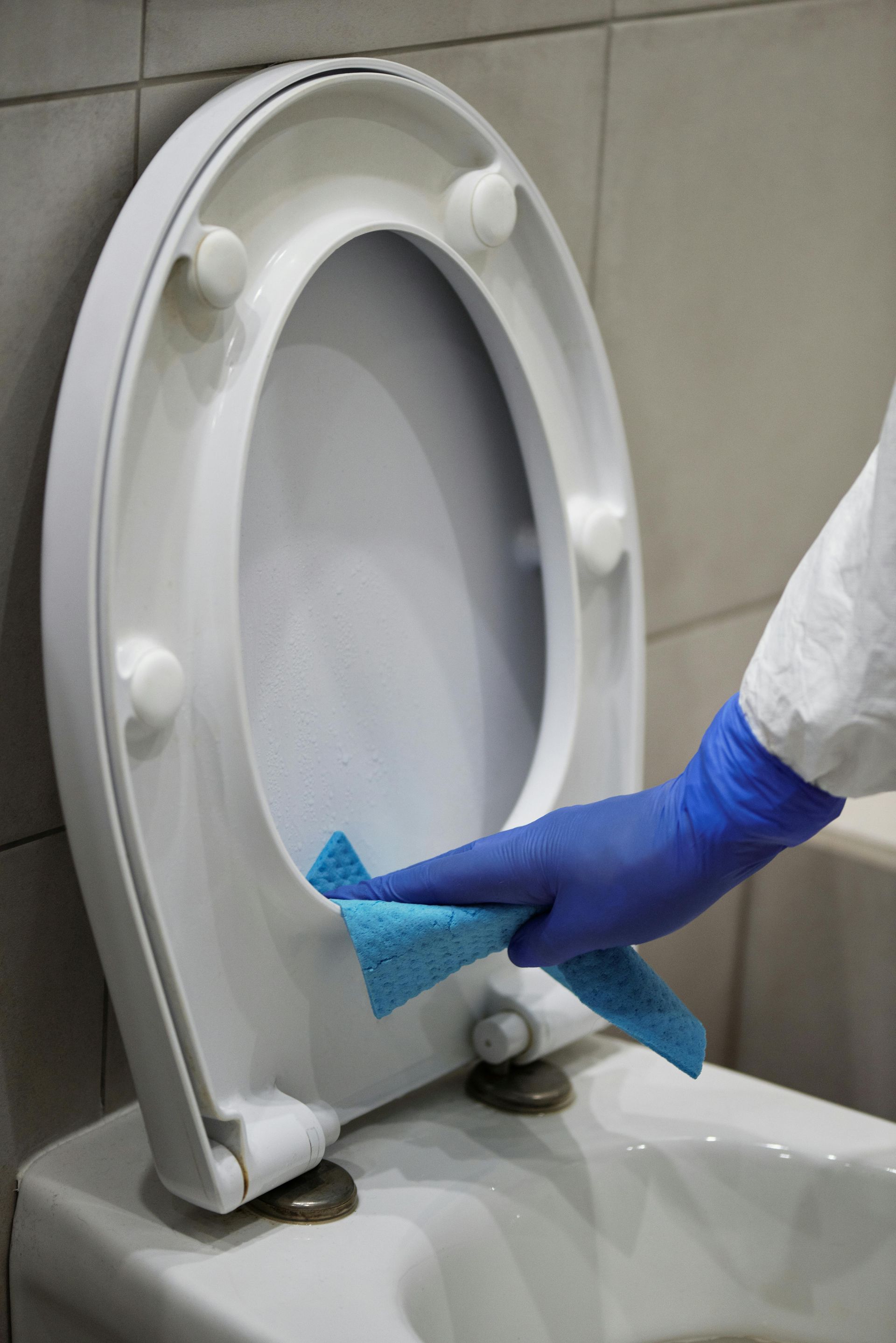 Person in blue glove wiping a toilet seat with a blue cloth in a bathroom.