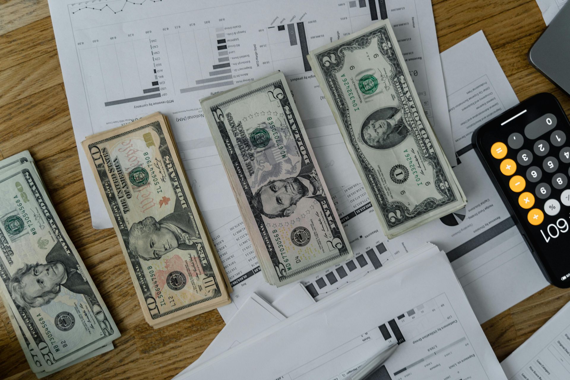 Bundles of US currency, calculator, and financial documents on a wooden surface.