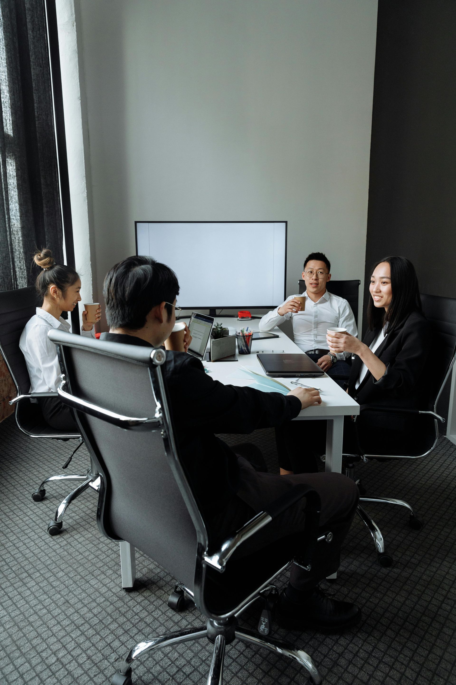 People in a meeting room, sitting at a white table with a screen behind them.