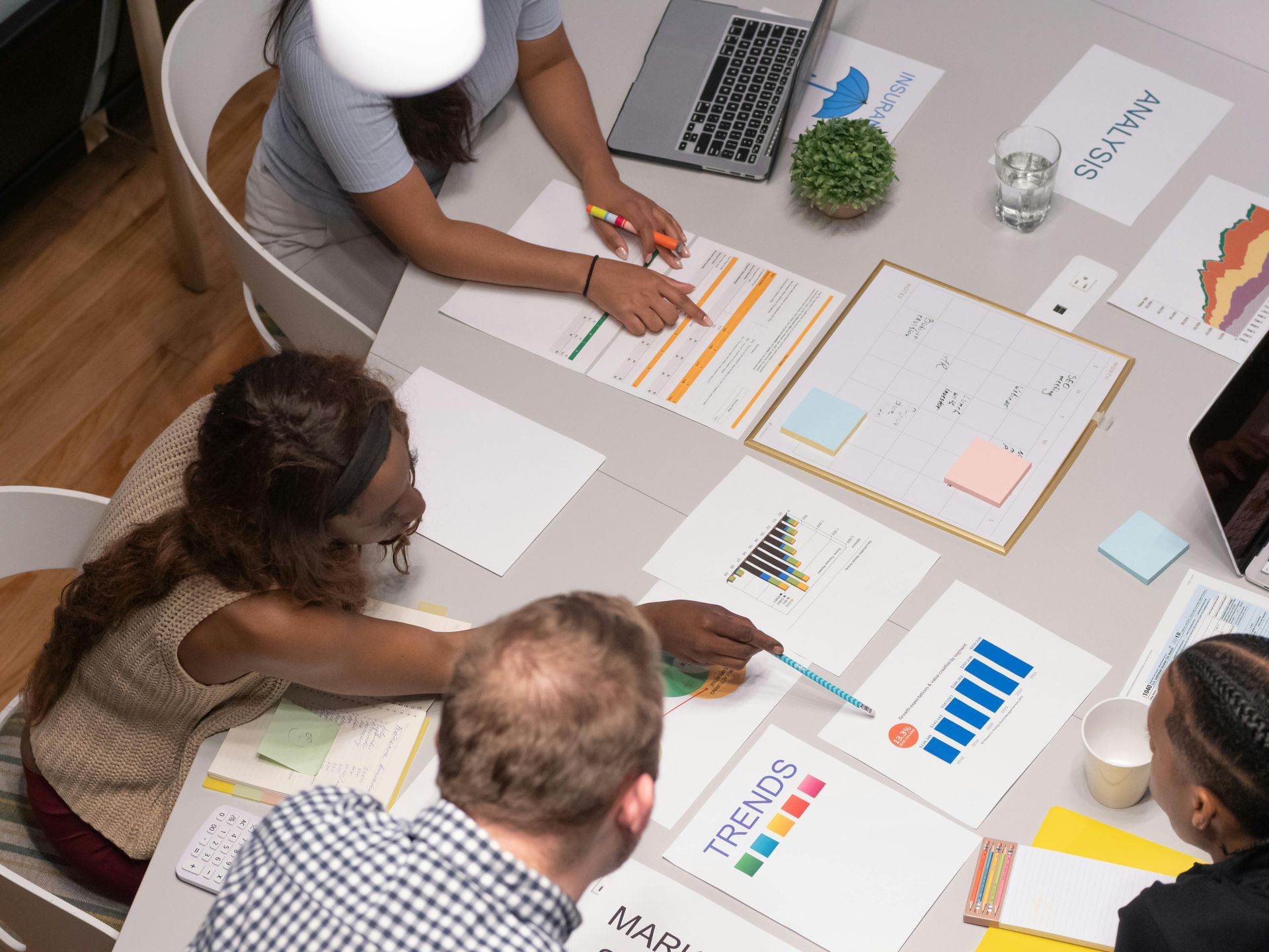 People at a table, reviewing documents and graphs. Some are pointing at charts and using a laptop in an office.