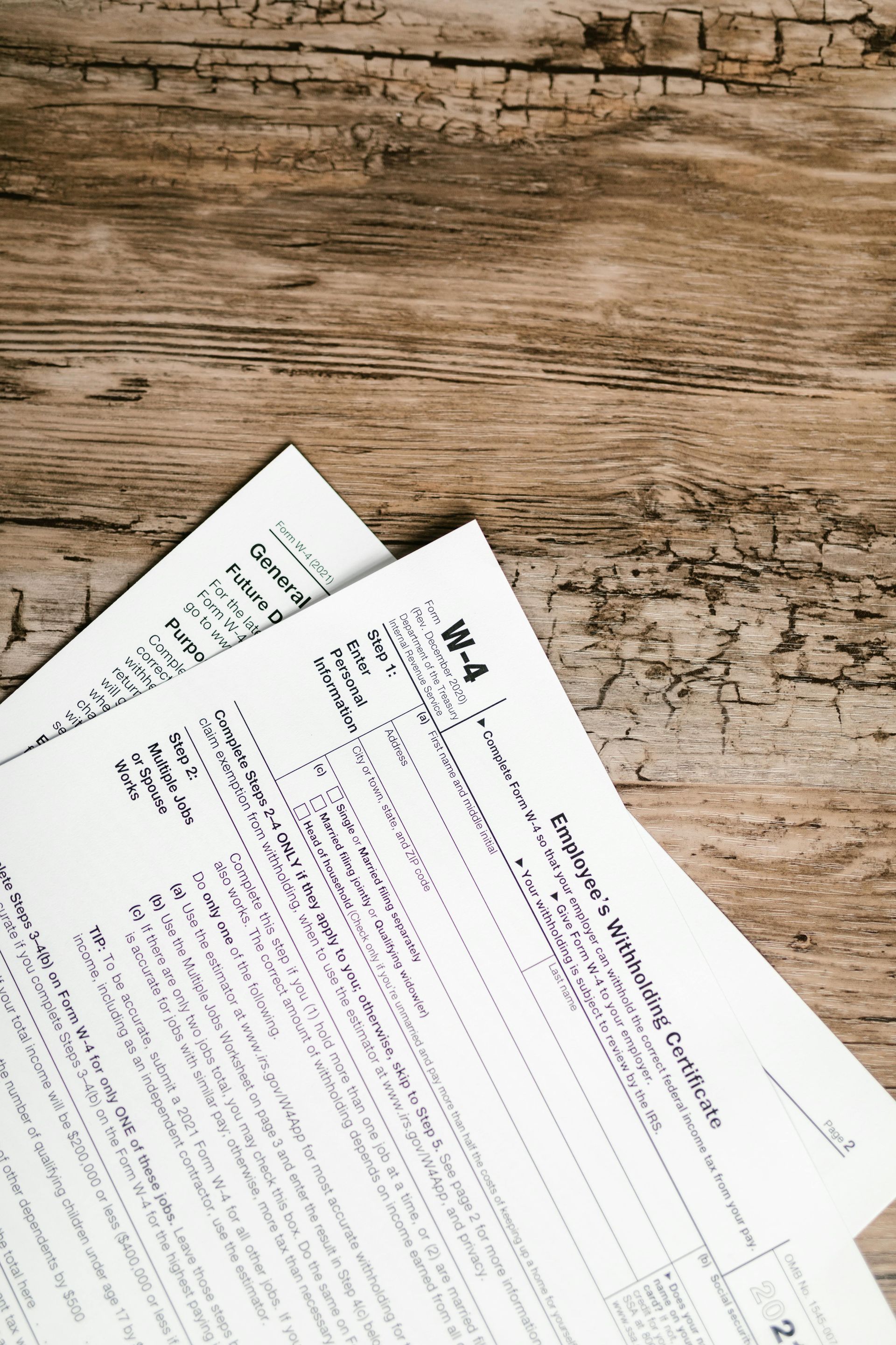 Two white W-4 tax forms on a weathered wooden surface, documents slightly overlapping.