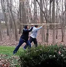 A man and a woman are holding sticks in the woods.