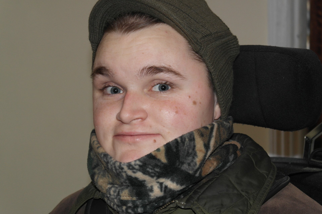 A young man wearing a hat and scarf is sitting in a wheelchair.