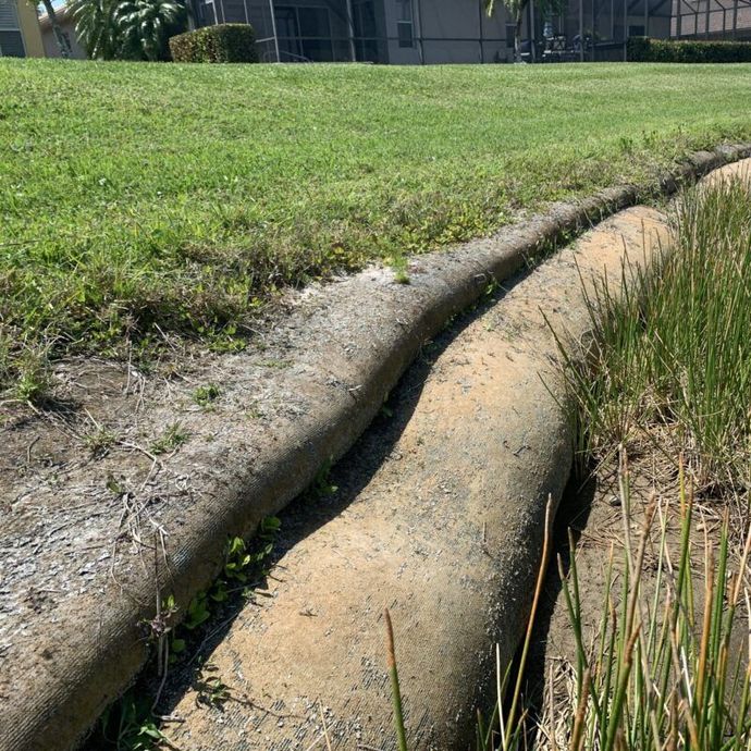 Two long, beige sandbags border grassy lawn and a pond edge.