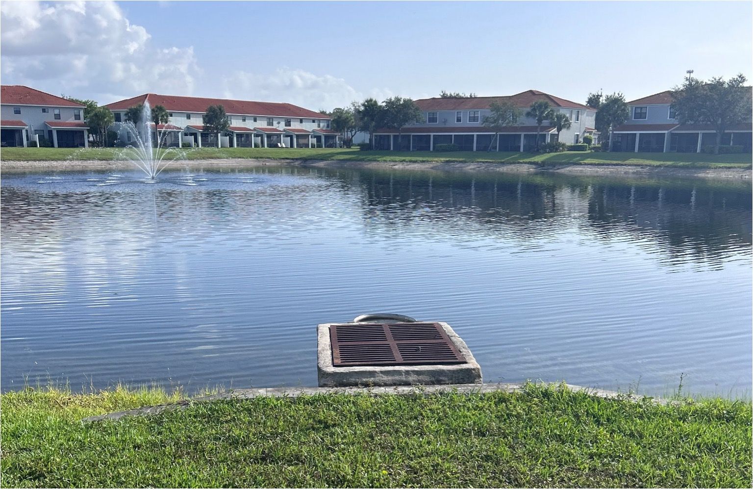 A tranquil lake with a fountain and surrounding townhouses. A concrete structure is in the water.