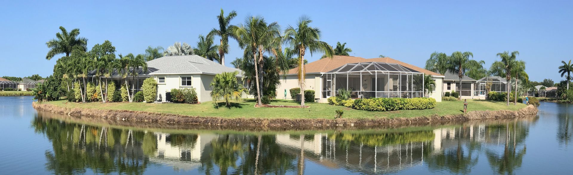 Houses on an island surrounded by water, palm trees, and a clear blue sky.
