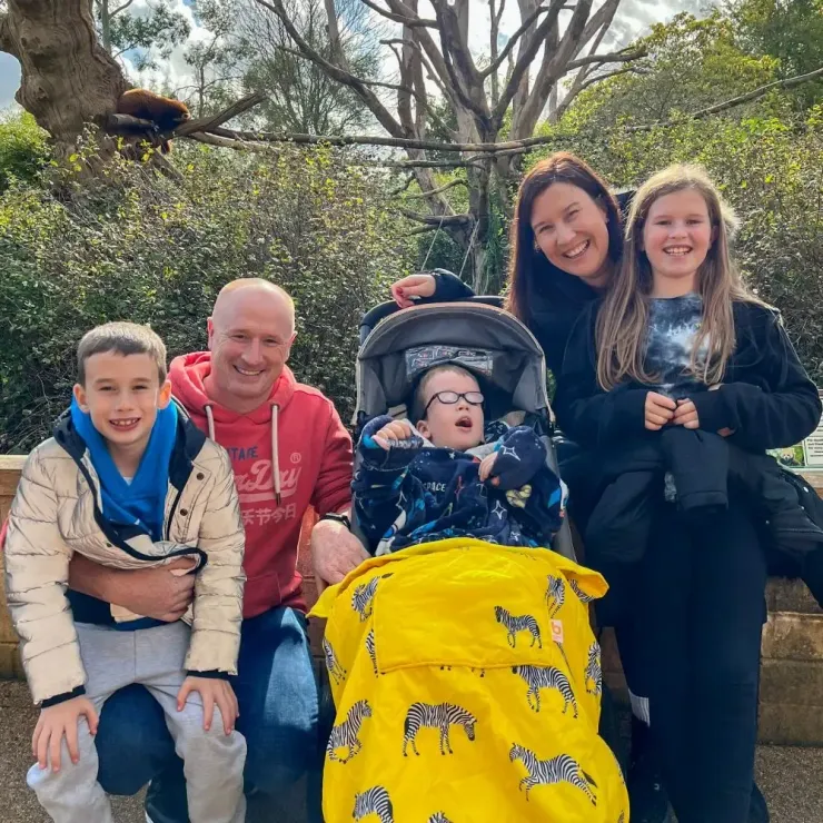 Family of five outdoors, smiling around a child in a stroller with a bright yellow blanket.