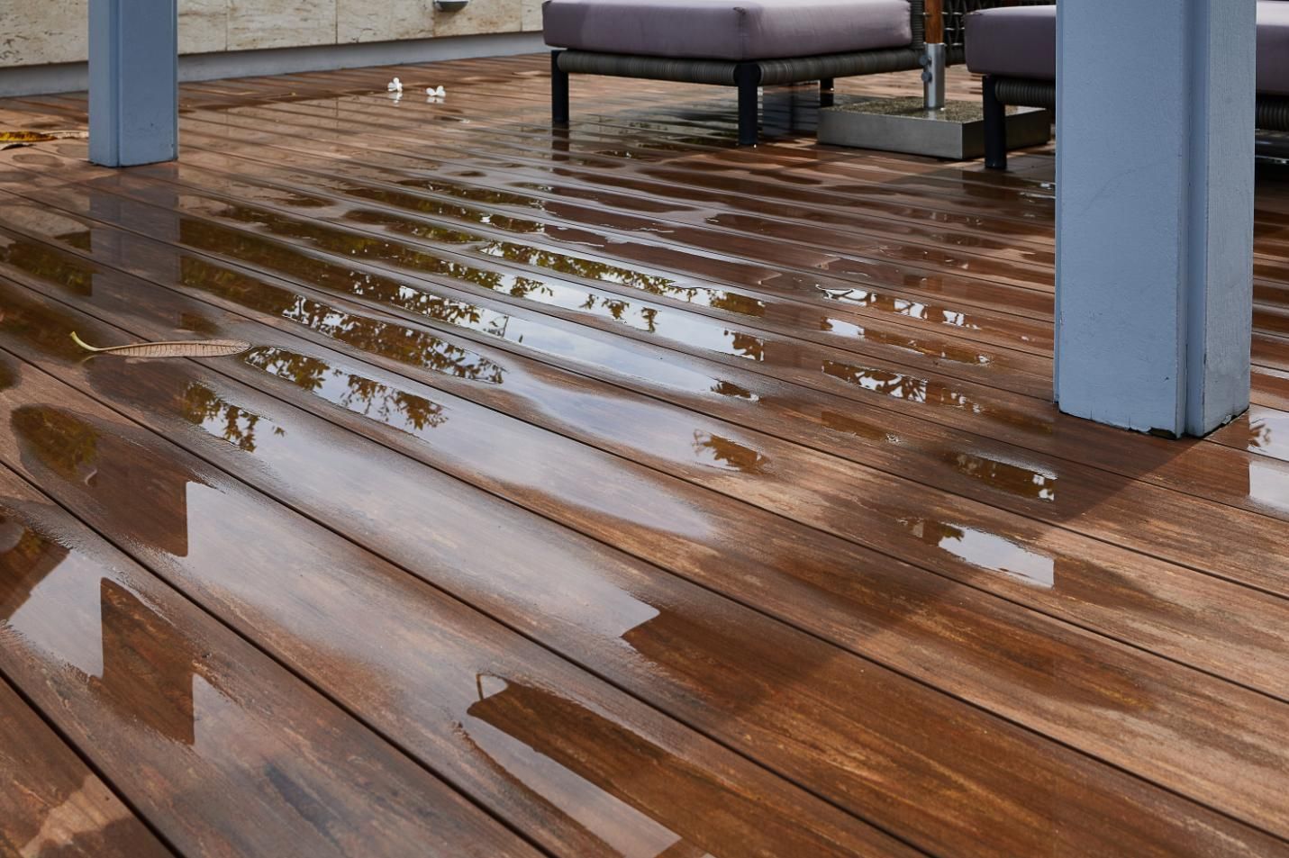 Rainwater puddles on a wet wooden deck surface with parts of patio furniture.