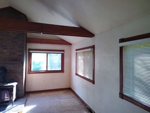 A bright room with a brick fireplace, a wood stove, exposed wooden ceiling beams.