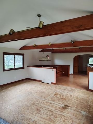 An empty room with exposed wooden ceiling beams, light-colored walls, wood-look flooring.