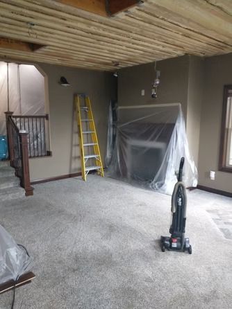 A room under renovation with a ladder, a vacuum, and a fireplace covered in plastic sheeting.