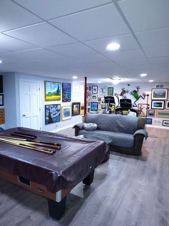 A finished basement with a pool table in the foreground, a couch, a treadmill, and walls.