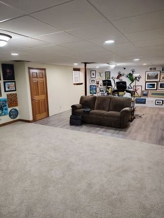 A carpeted basement with a brown sofa, a wooden door, and a gallery.