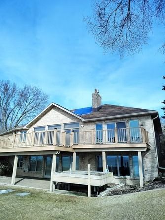 A two-story stone house with a large wooden deck and balcony.