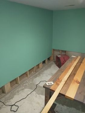 A basement room under renovation with teal painted walls, exposed wooden studs at the base.