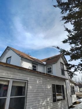 A two-story white house with light brown shingles under a blue.