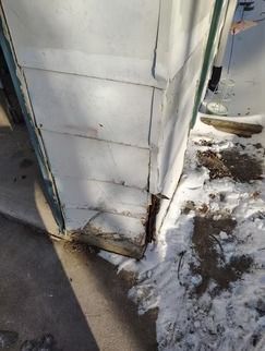A close-up of a damaged corner of a house exterior with peeling white siding.