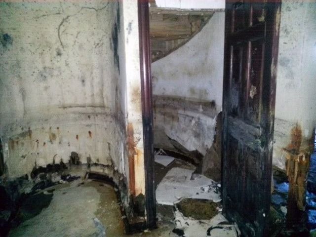 A dimly lit room with peeling, water-damaged walls and a dark wooden door.