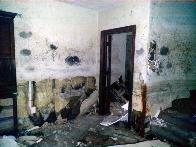 A dilapidated room with peeling, stained walls, exposed insulation, and debris covering.