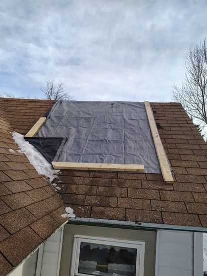 A gray tarp covering a section of a brown shingled roof.
