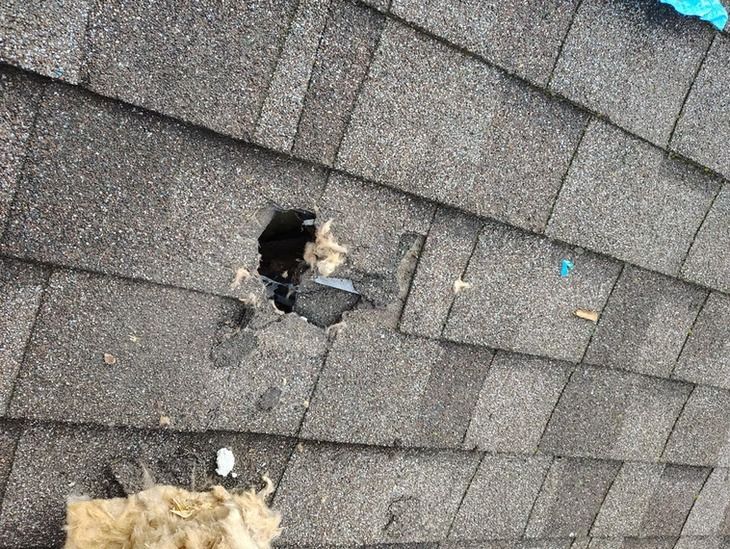 A damaged gray shingle roof featuring a hole.