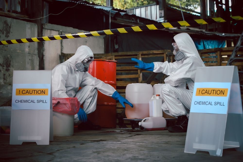 A person in a white lab coat and blue gloves carries a red biohazard waste bag.