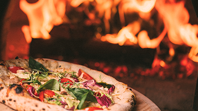 A pizza is sitting on a wooden table in front of a pizza oven.