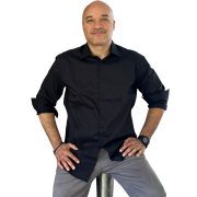 Man standing with hands on hips, wearing a black shirt and gray pants against a white background