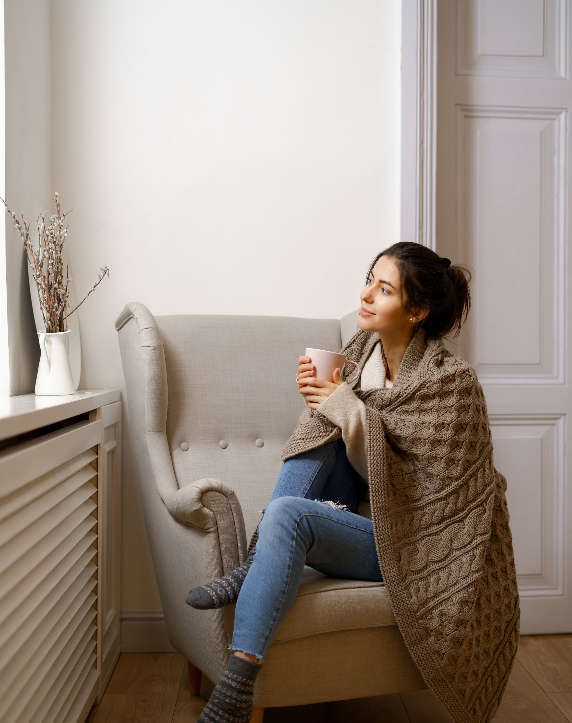 Una donna avvolta in una coperta è seduta su una sedia e tiene in mano una tazza di caffè.