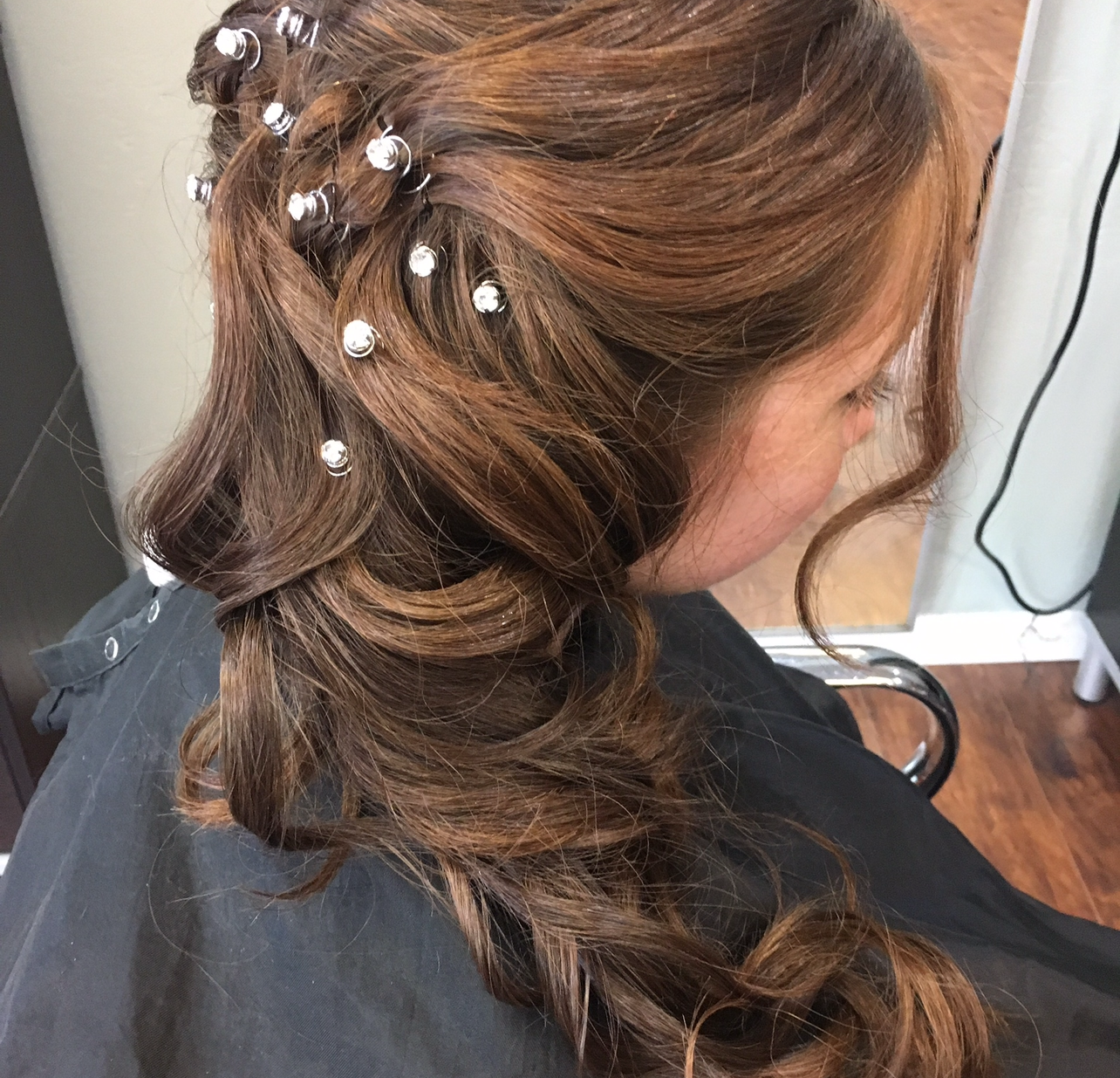 A woman is sitting in a chair with her hair in a half up half down hairstyle.