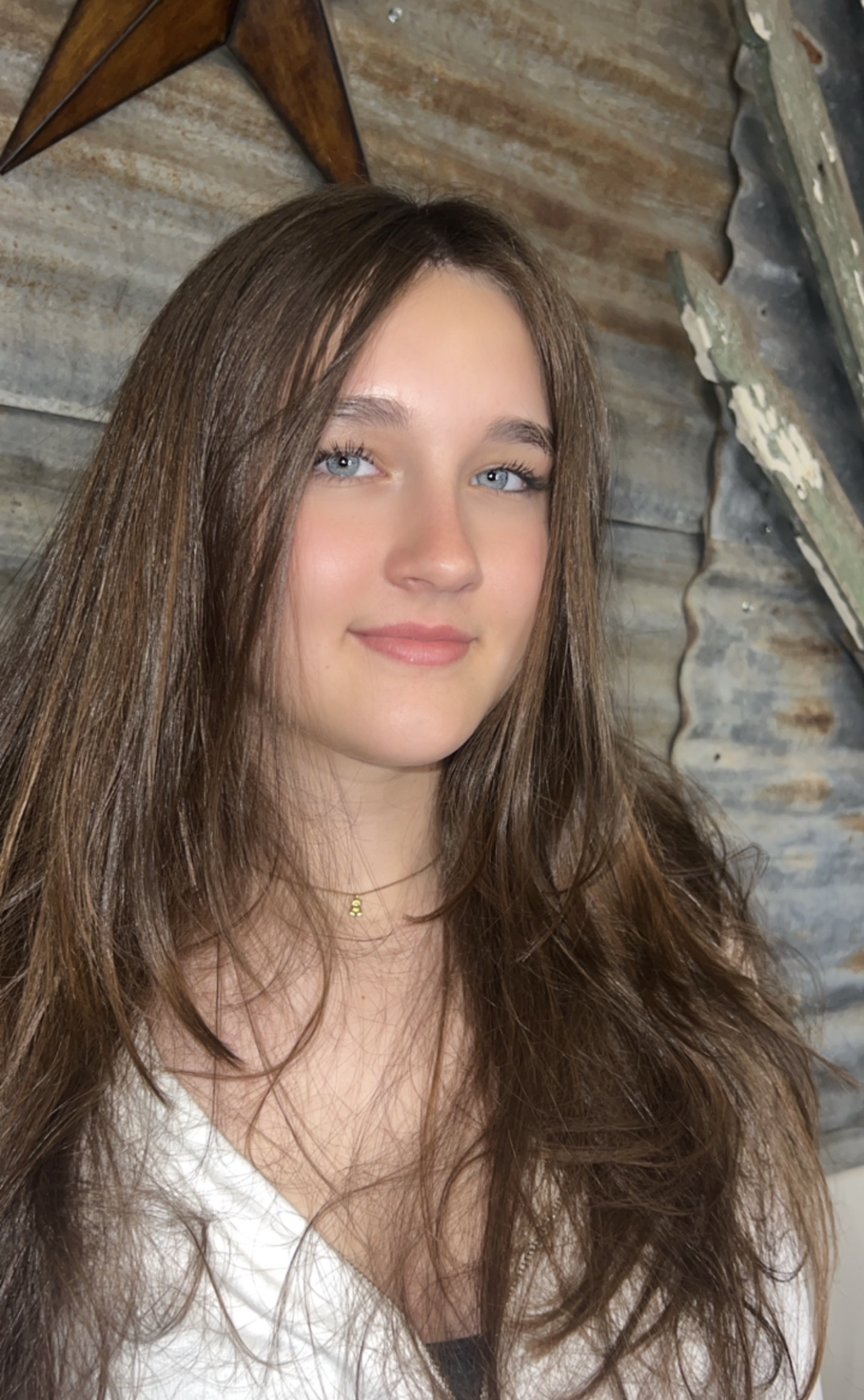 A young woman with long brown hair and blue eyes is smiling for the camera.