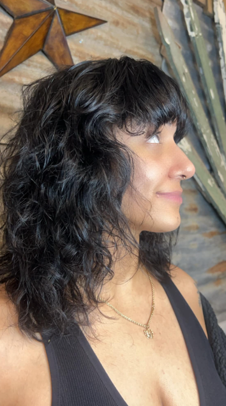 A woman with curly hair and bangs is wearing a black tank top.
