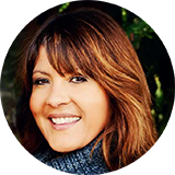 A woman with long brown hair and bangs is smiling in a circle.