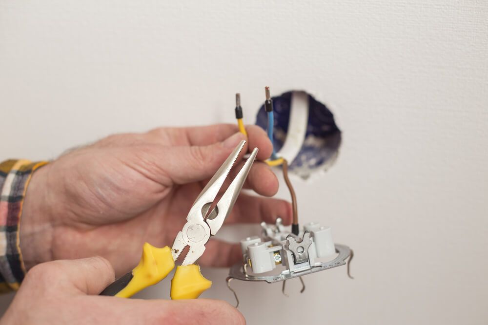 A Person is Fixing a Light Switch With Pliers — Bangalow Electrical in Bangalow, NSW