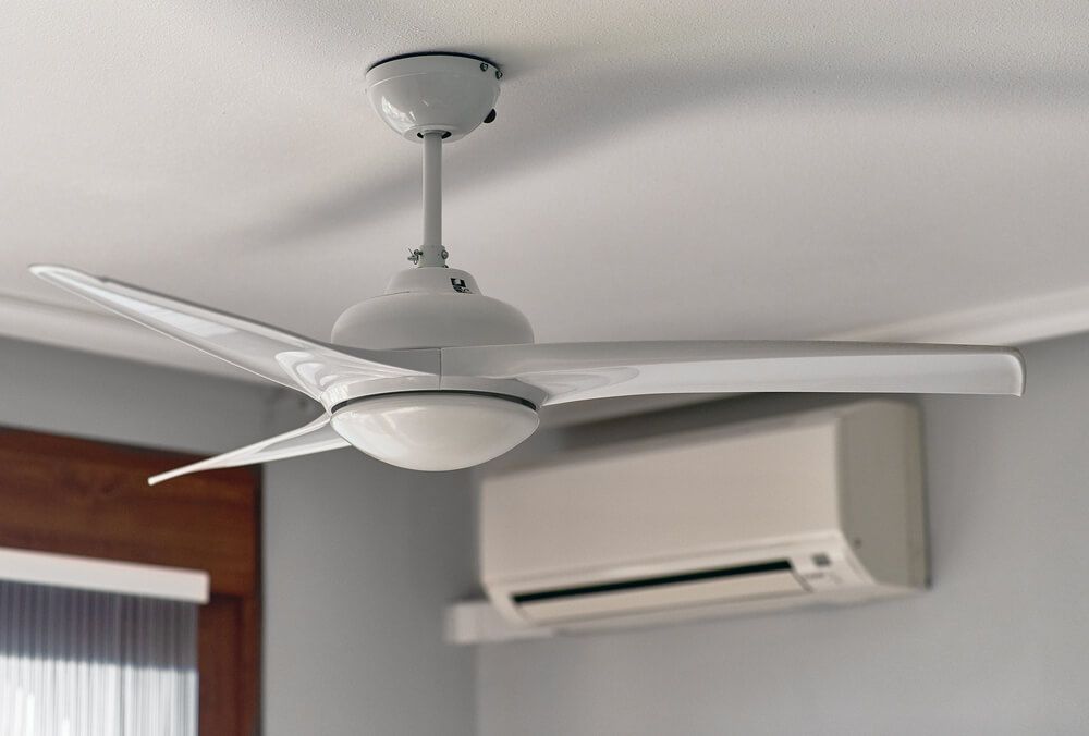 A White Ceiling Fan is Hanging From the Ceiling in a Room Next to an Air Conditioner — Bangalow Electrical in Bangalow, NSW