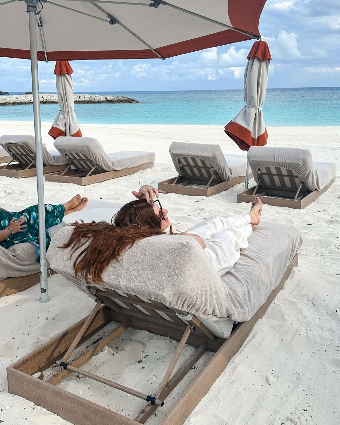 Beachside cabana with cushioned lounge beds under a canopy, facing turquoise ocean and sandy shore.