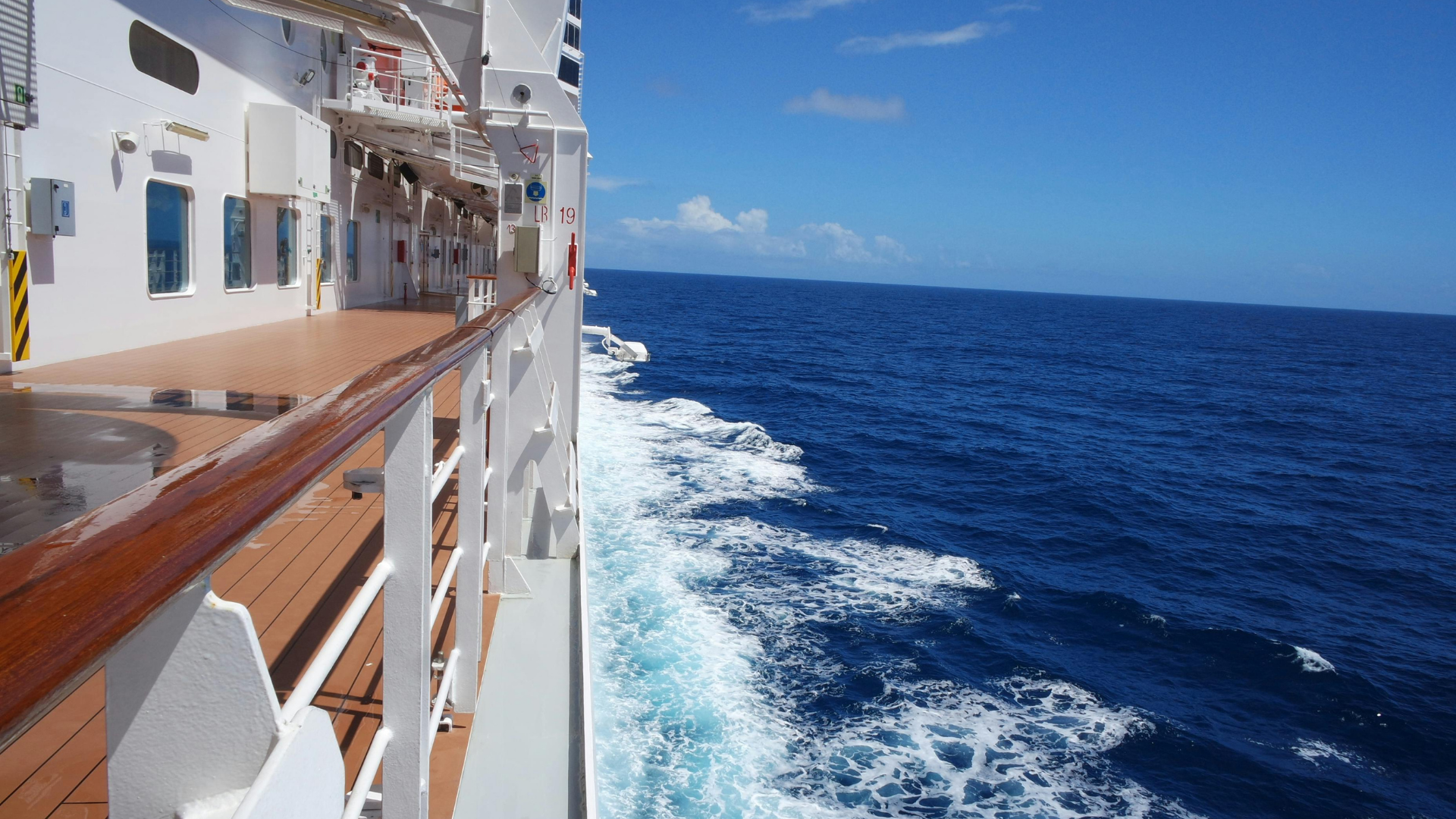 Ship deck beside deep blue ocean under a clear sky, with white wake trailing alongside.