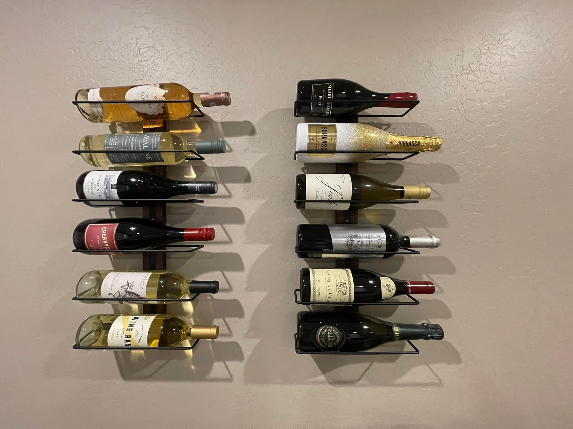 Two wall-mounted wine racks holding various wine bottles against a beige wall.