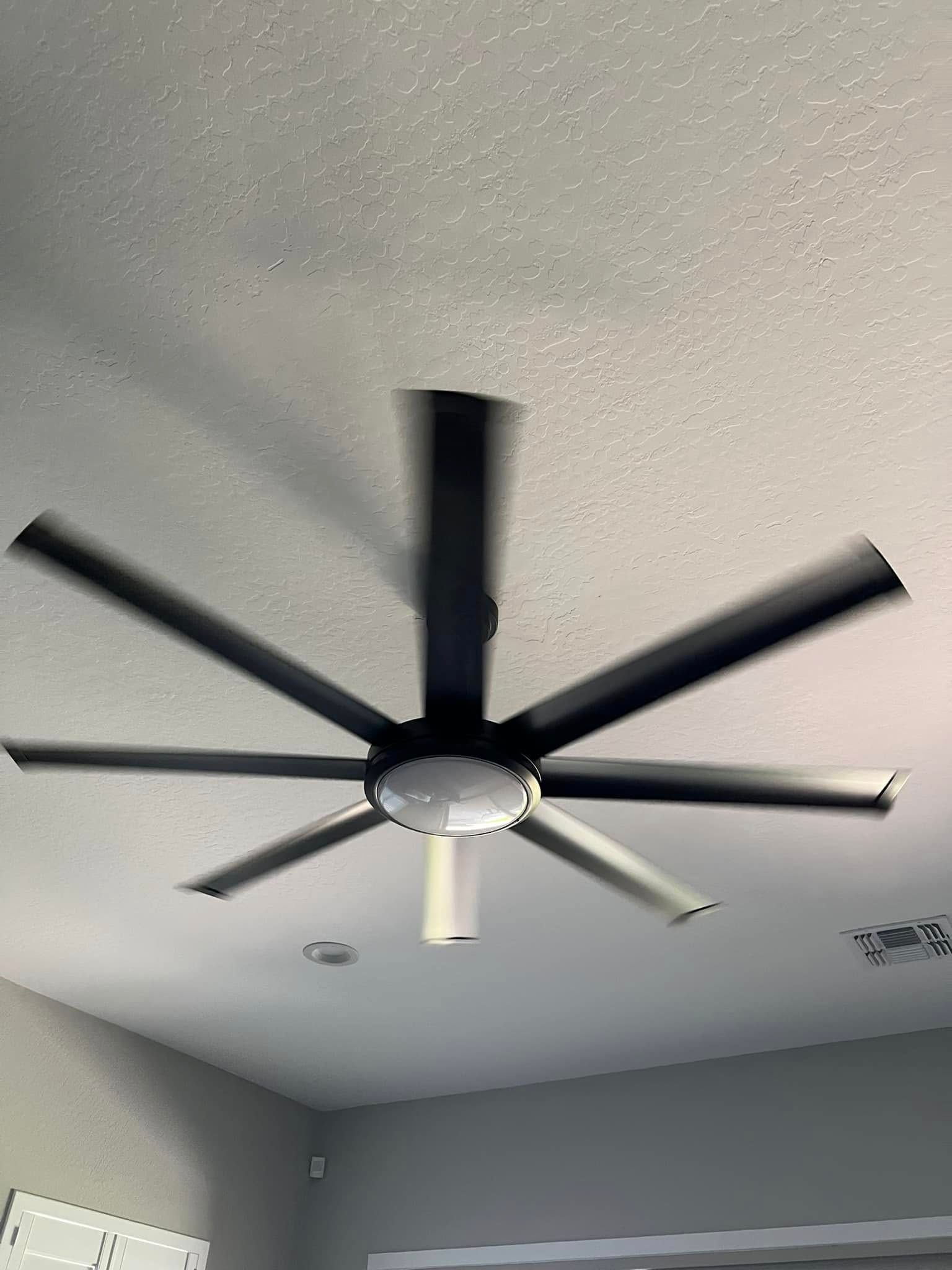 Ceiling fan with eight black blades, spinning, centered in a white ceiling.
