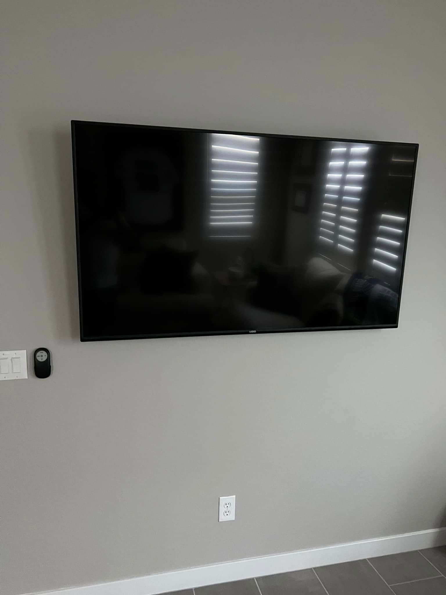 A large, black flat-screen TV mounted on a gray wall; a remote is to the left.