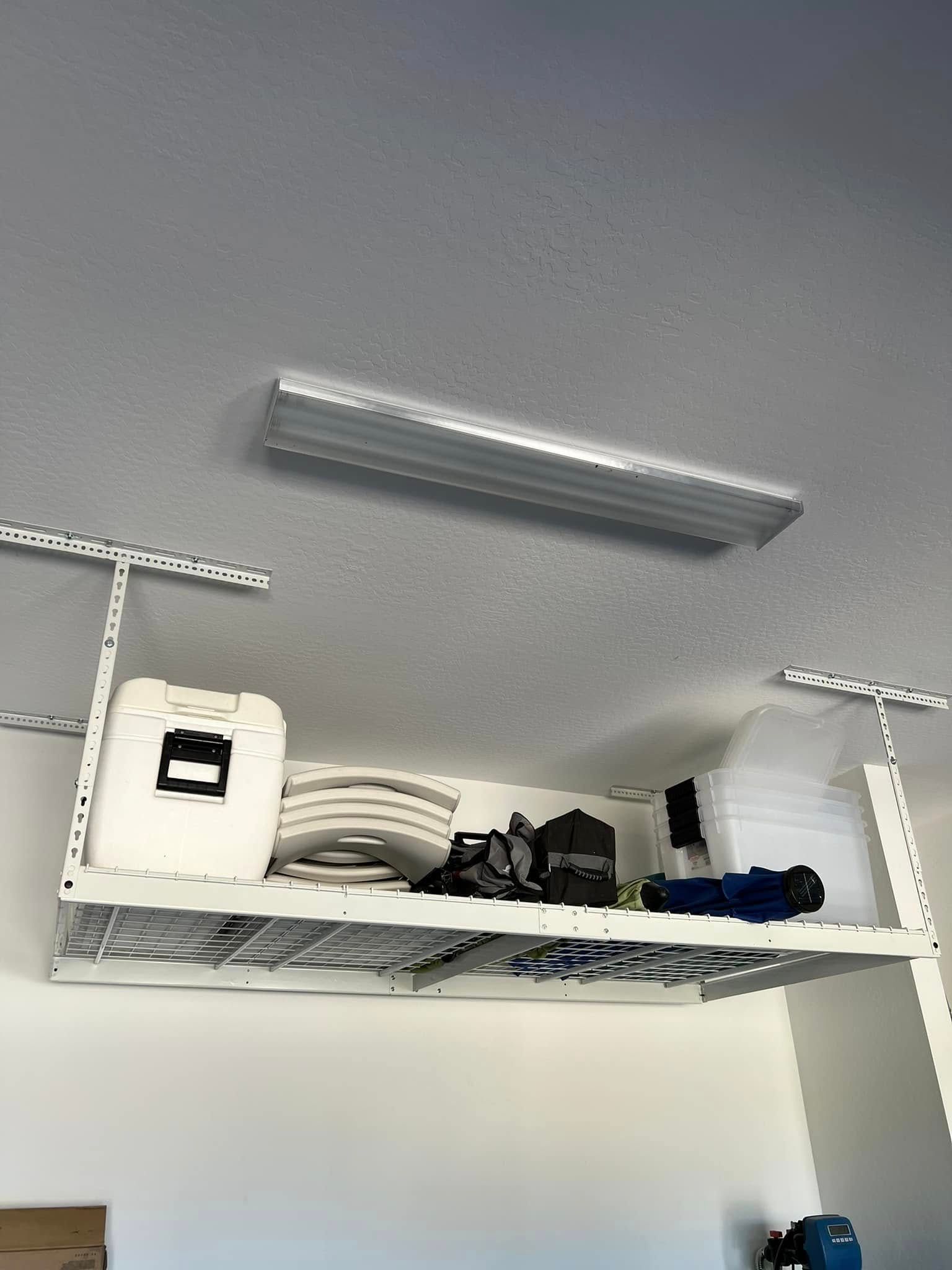 Overhead garage shelf holding various items, below a ceiling light.