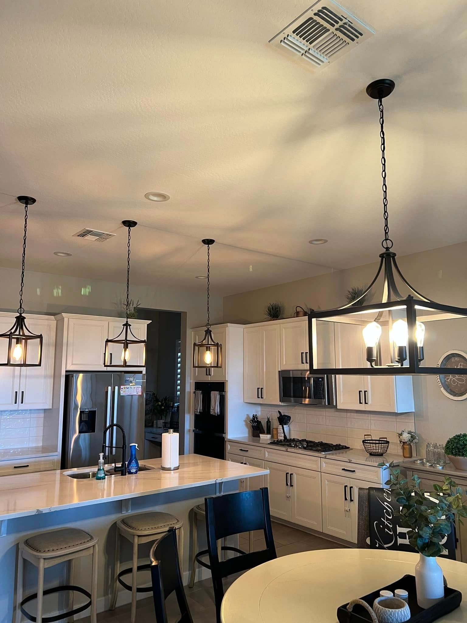 Kitchen with white cabinets, stainless steel appliances, and pendant lights over a countertop island and dining table.