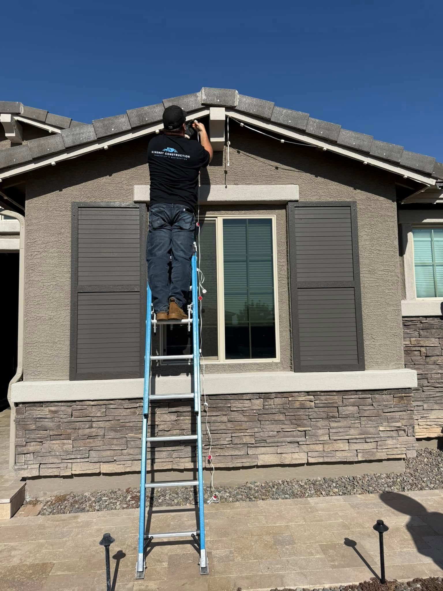 Person on ladder installing lights on house roof.