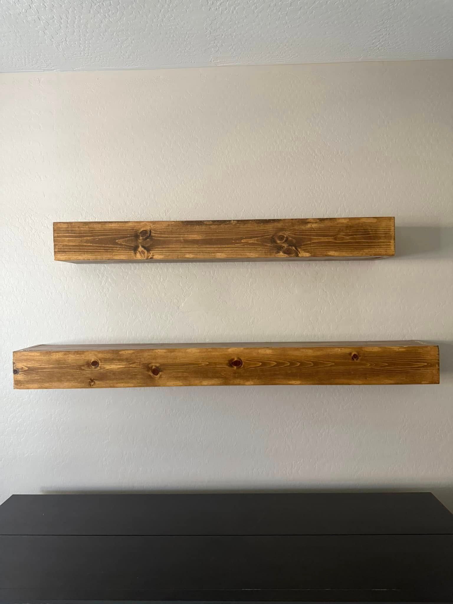 Two stained wooden shelves mounted on a light gray wall above a black cabinet.