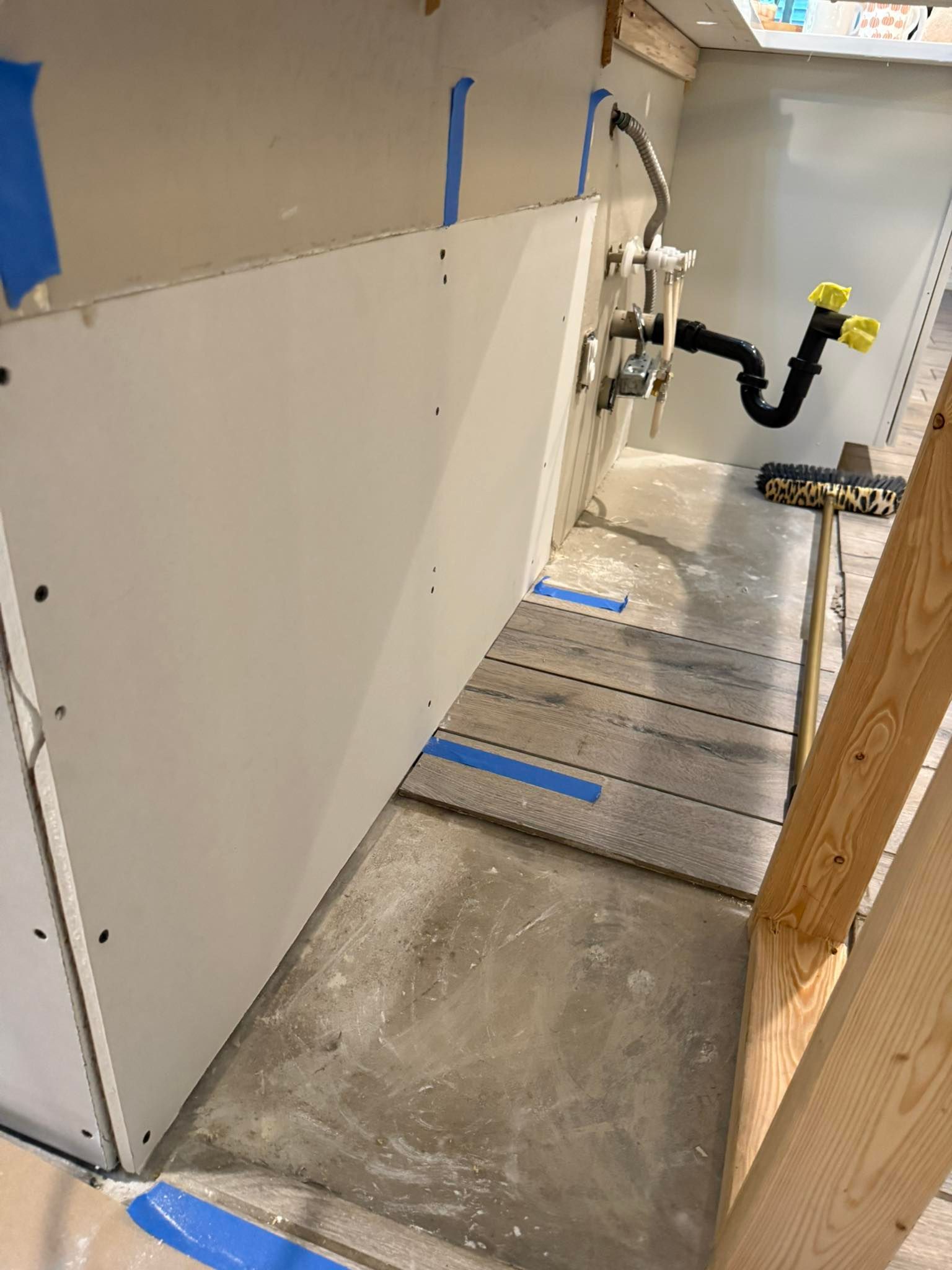 Interior of a bathroom under construction. Drywall installed; plumbing visible. Cement floor with tile laid.