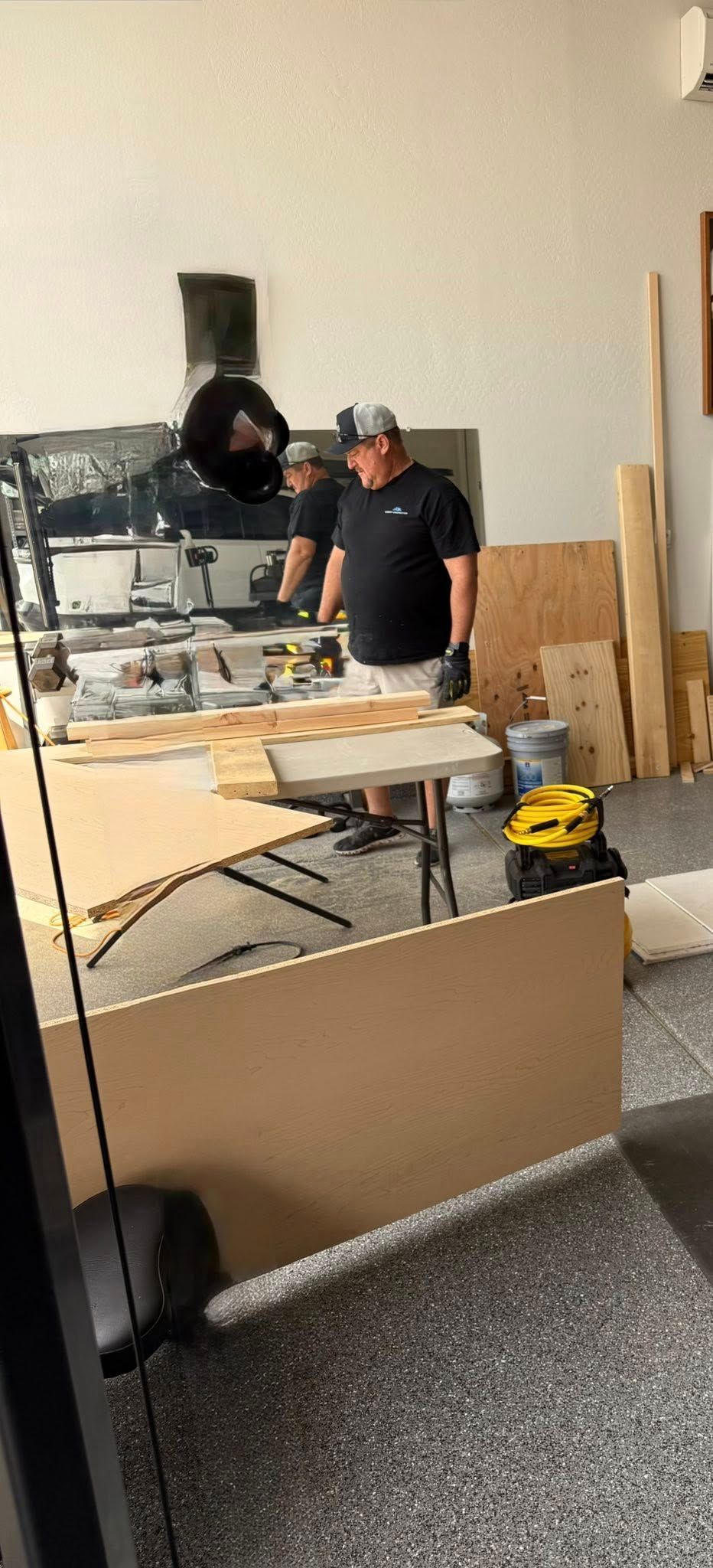 A man in a workshop stands near a partially built, curved wooden desk; several tools are nearby.