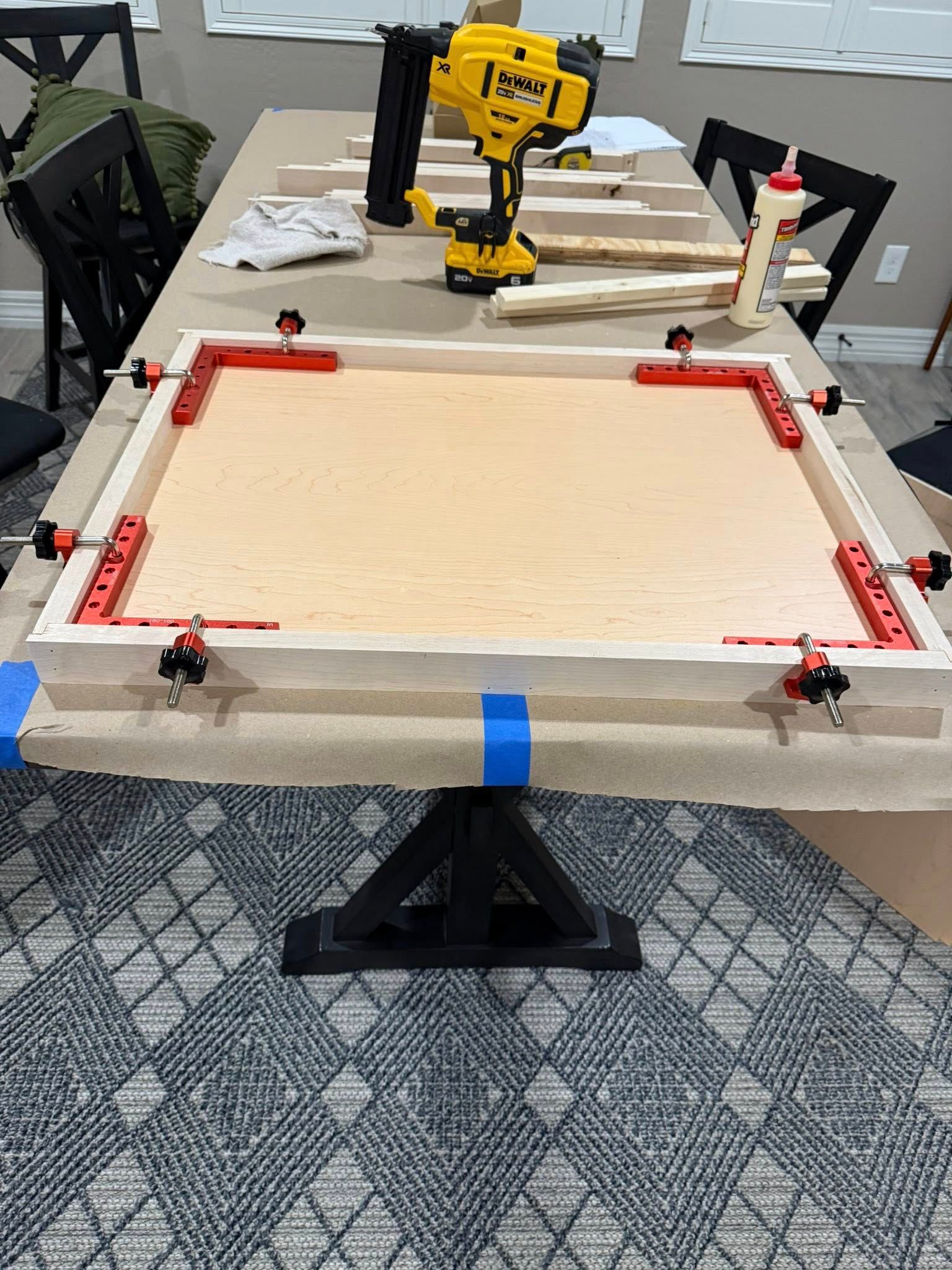 Wooden frame being assembled on a table using clamps and woodworking tools.