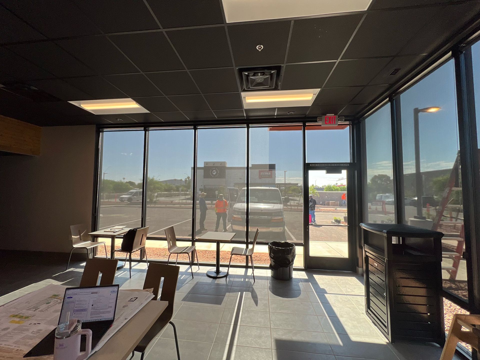 Interior of a restaurant with tables, chairs, and large windows looking out onto a parking lot.