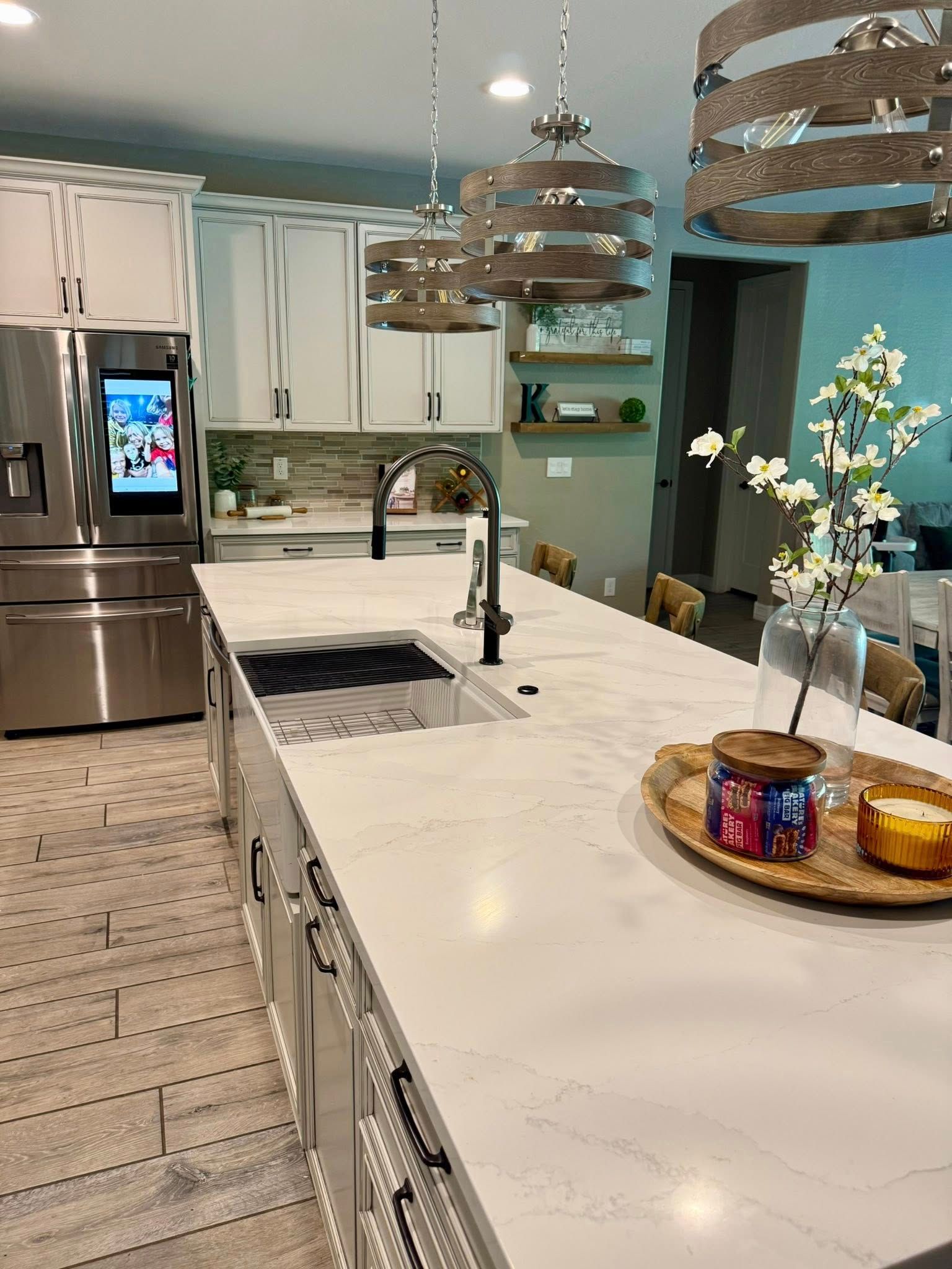 Modern kitchen with white countertops, island, and pendant lights. A stainless steel refrigerator is visible.