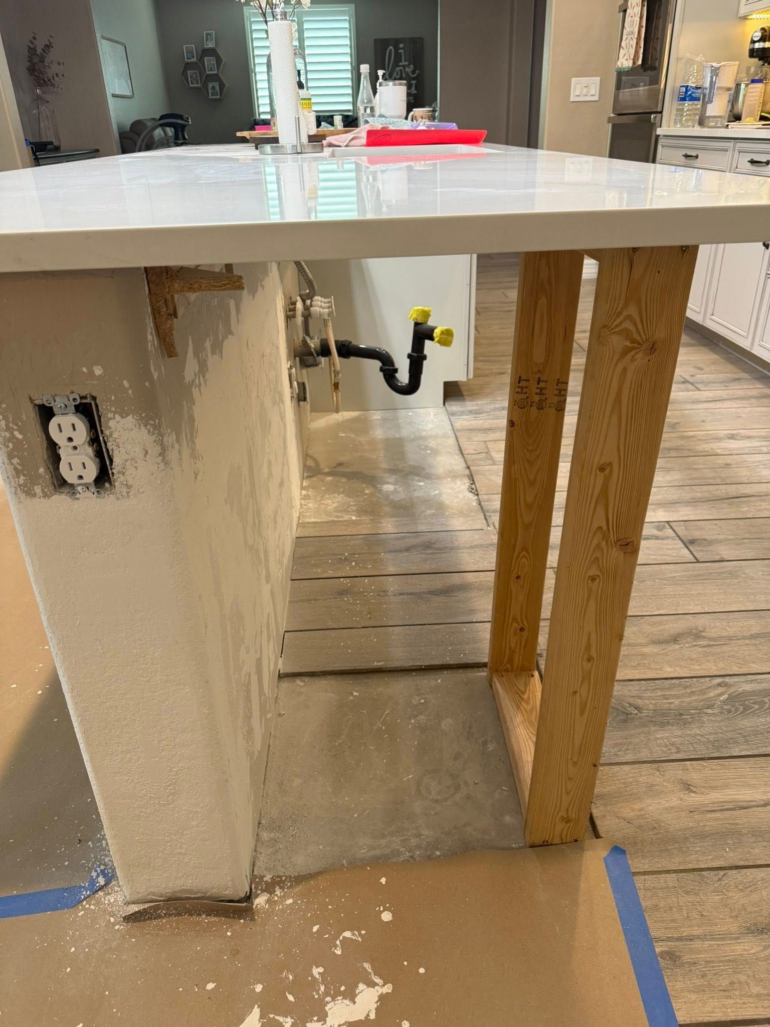 Kitchen island under construction with exposed plumbing, support beams, and drywall.